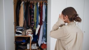 mulher olhando preocupada para guarda-roupa cheio e bagunçado